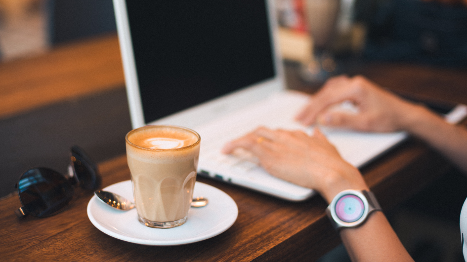 mujer escribiendo en la computadora y tomando cafe